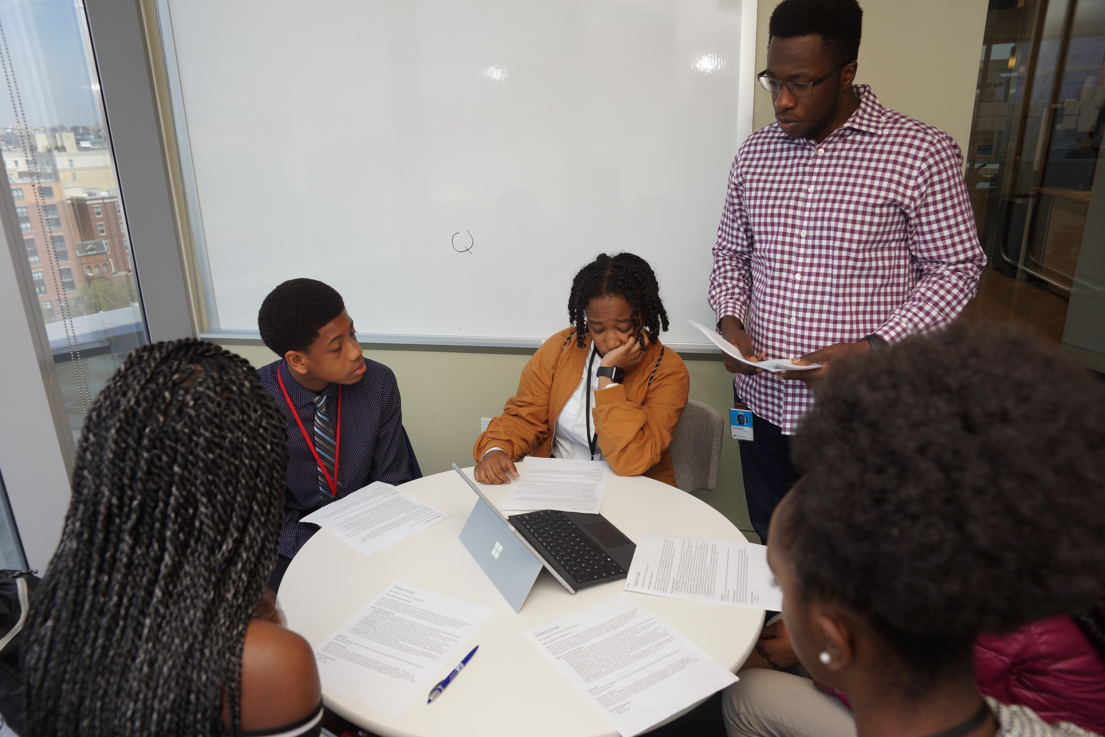 High school students working together at a table while a mentor provides guidance